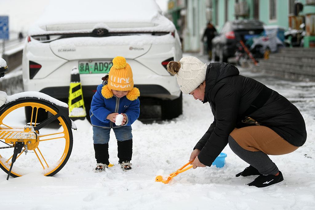 2023年12月11日，北京迎来降雪，家长带着孩子正在雪中嬉戏。人民网记者 于凯摄
